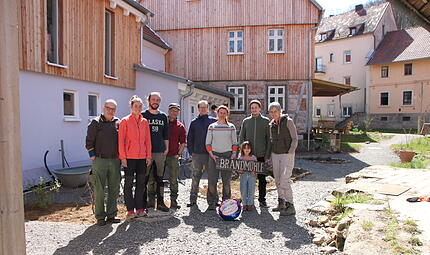 Bewohner der Brandmühle bei Maßbach / Poppenlauer Auf dem Foto von links stehen vor den Wohnhäusern und der Mühle: Klaus Reichert, Anna Baumgartner, Simon Memmel, Rainer Neubauer, André und Magdalena Glöckner, Jakob mit Kind sowie Martina Neubauer.