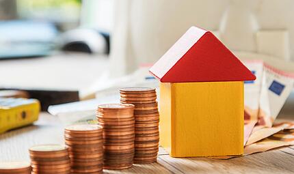 Münzen und ein Haus aus Bausteinen liegen auf einem Tisch Münzen und ein Haus aus Bausteinen liegen auf einem Tisch